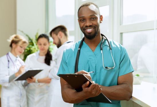 Smiling healthcare professional with colleagues in the background, hired by a healthcare staffing agency.